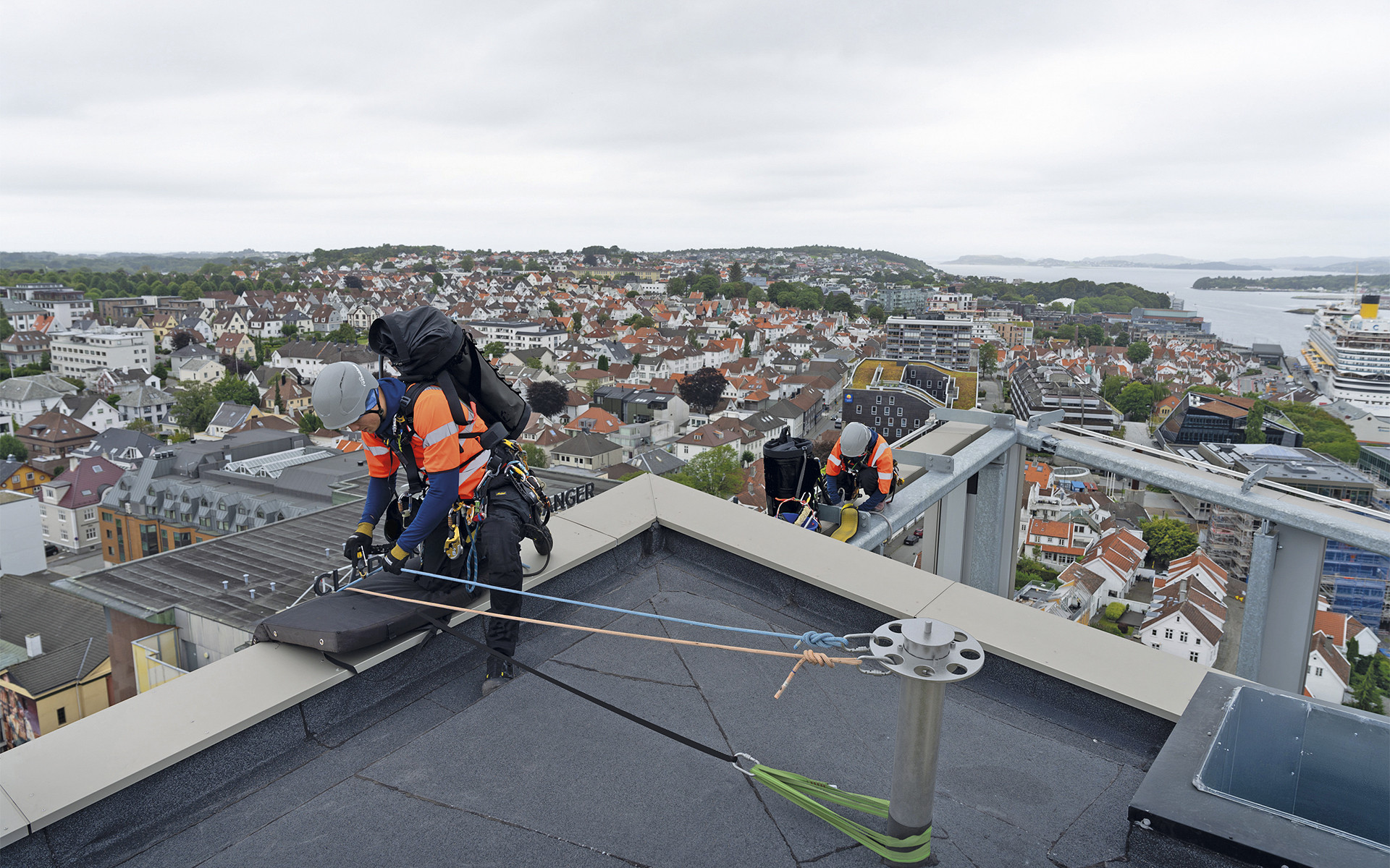Workers performing anchorage operations on a multi-storey building roof, wearing Rothoblaas HERO safety helmets and fall protection systems